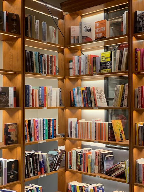 The image features a well-organized wooden bookshelf filled with a variety of hardcover and paperback books, arranged in multiple rows across several vertical compartments. The books include titles on